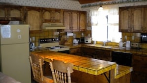 A kitchen with wooden cabinets, a stove, a refrigerator, and a tiled island with chairs. - 842 Cirugu (South Lake Tahoe)