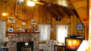 A cozy cabin interior with a stone fireplace, wooden walls, a ceiling fan, and a television. - 3663 Forest Ave (South Lake Tahoe)