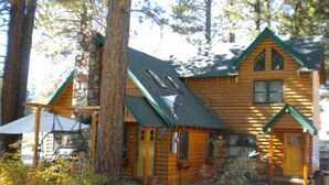 A log cabin with a green roof, a stone foundation, and a porch with a bench. - 3663 Forest Ave (South Lake Tahoe)