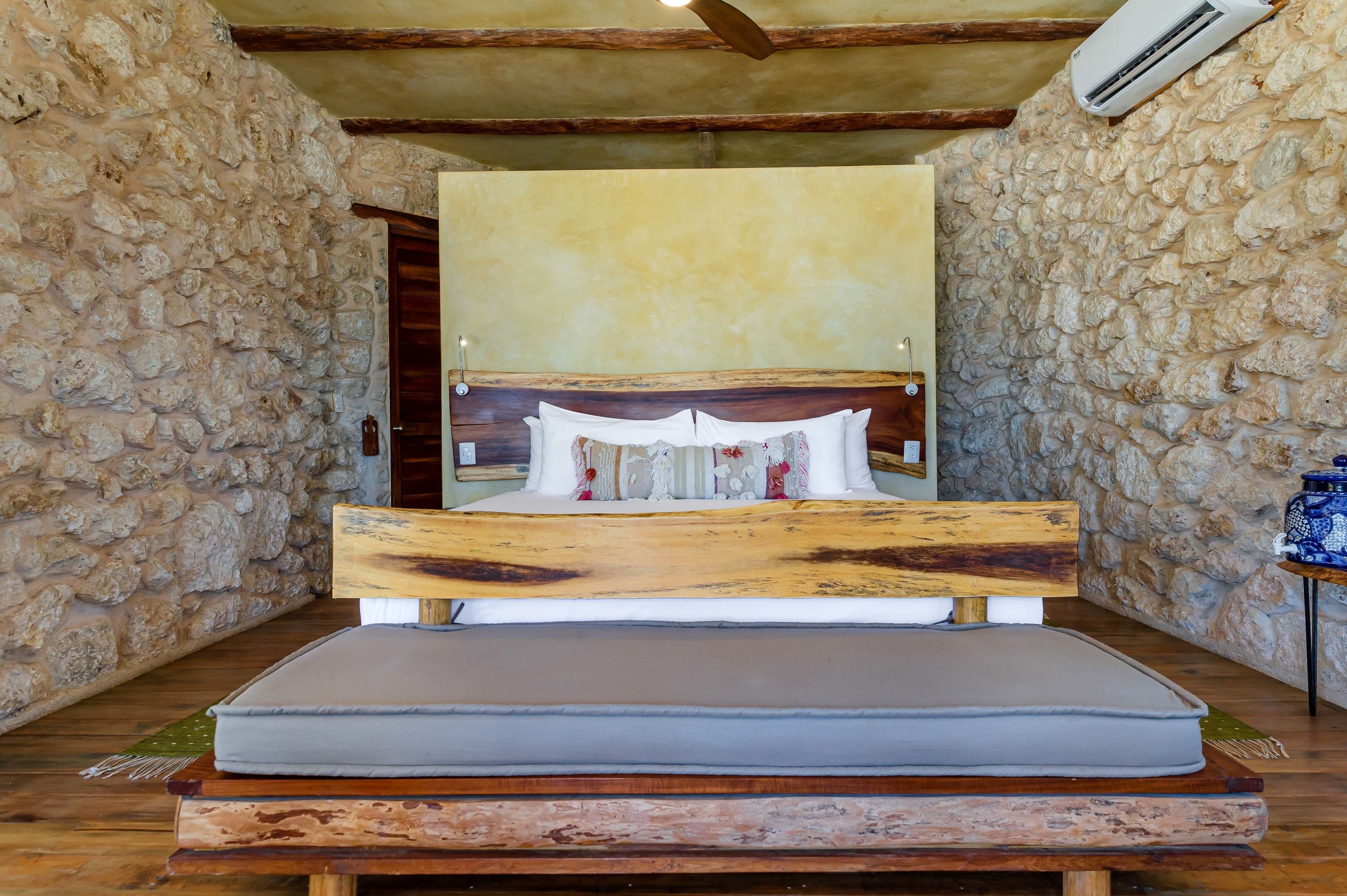 A rustic bedroom with a stone wall, wooden bed frame, and a simple headboard.