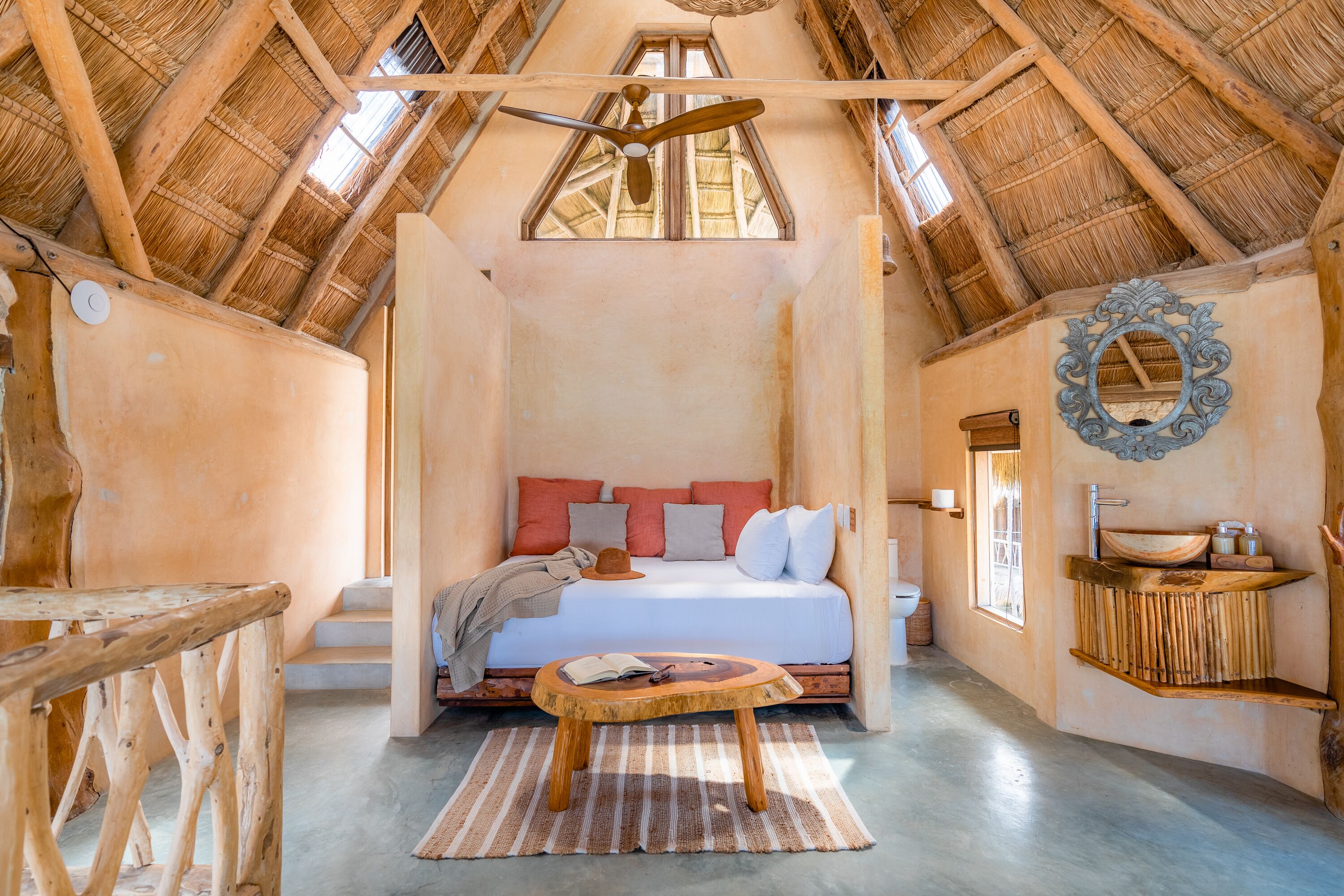 A rustic bedroom with a sloped ceiling, a bed with pillows, a wooden table, and a small window.