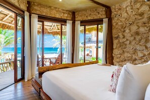 Un dormitorio con una cama grande, paredes de piedra y vistas a la playa y al océano.