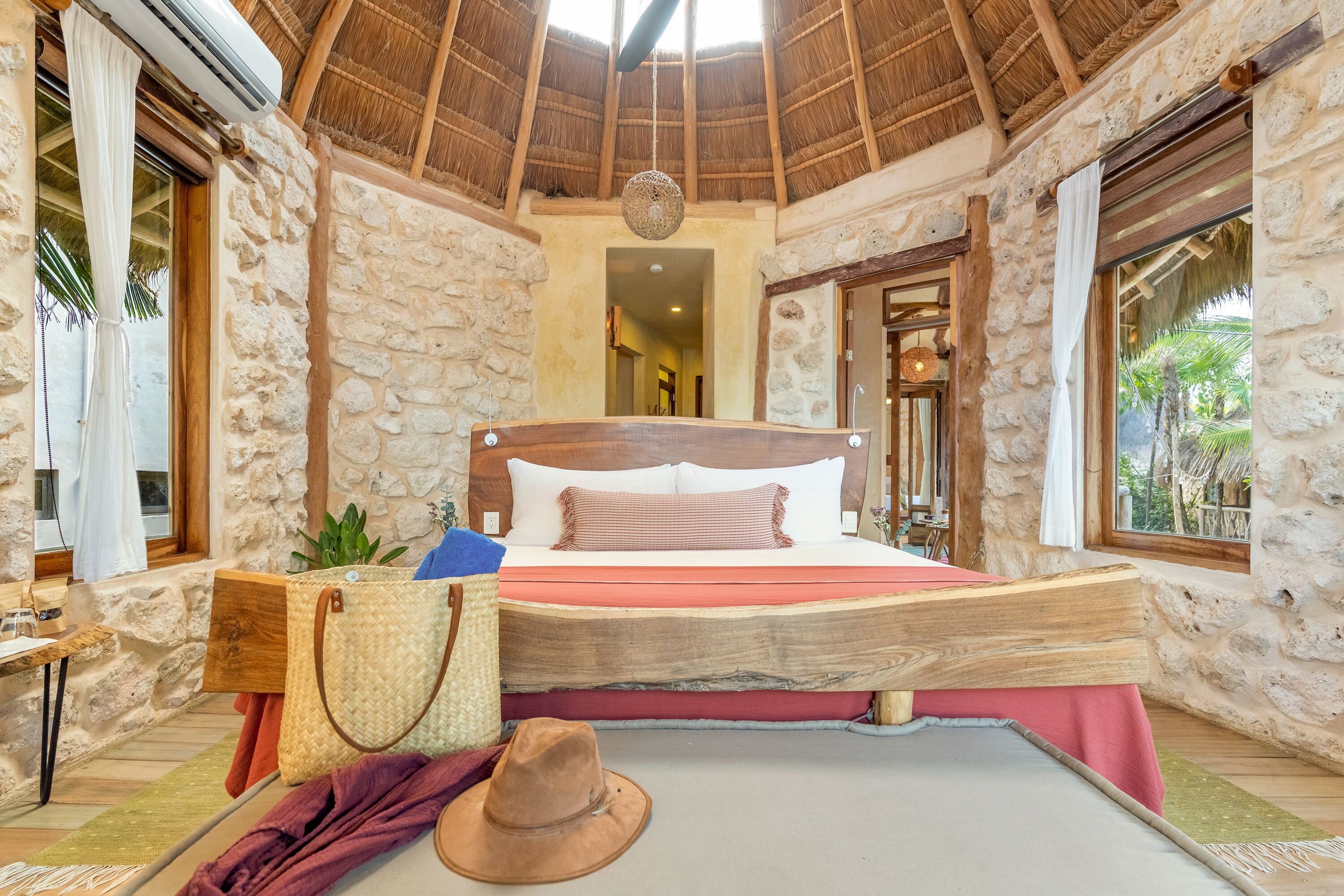 Ein Schlafzimmer mit Steinsandsteinwänden, einem hölzernen Bett, einer Pendelleuchte und Blick ins Freie.