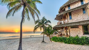 A beachfront hotel with a thatched roof, palm trees, and a view of the ocean at sunset. - Alaya Tulum (Tulum)