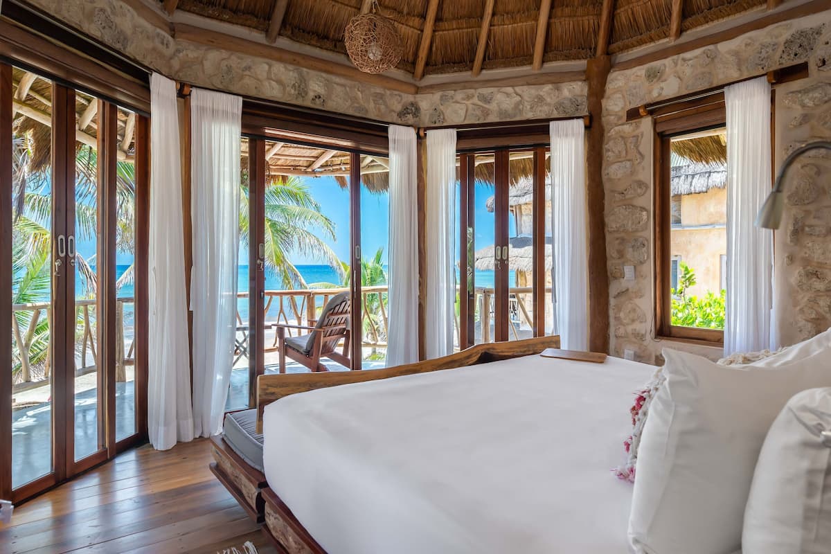 Un dormitorio con una cama grande, suelo de madera, paredes de piedra y vista al océano.