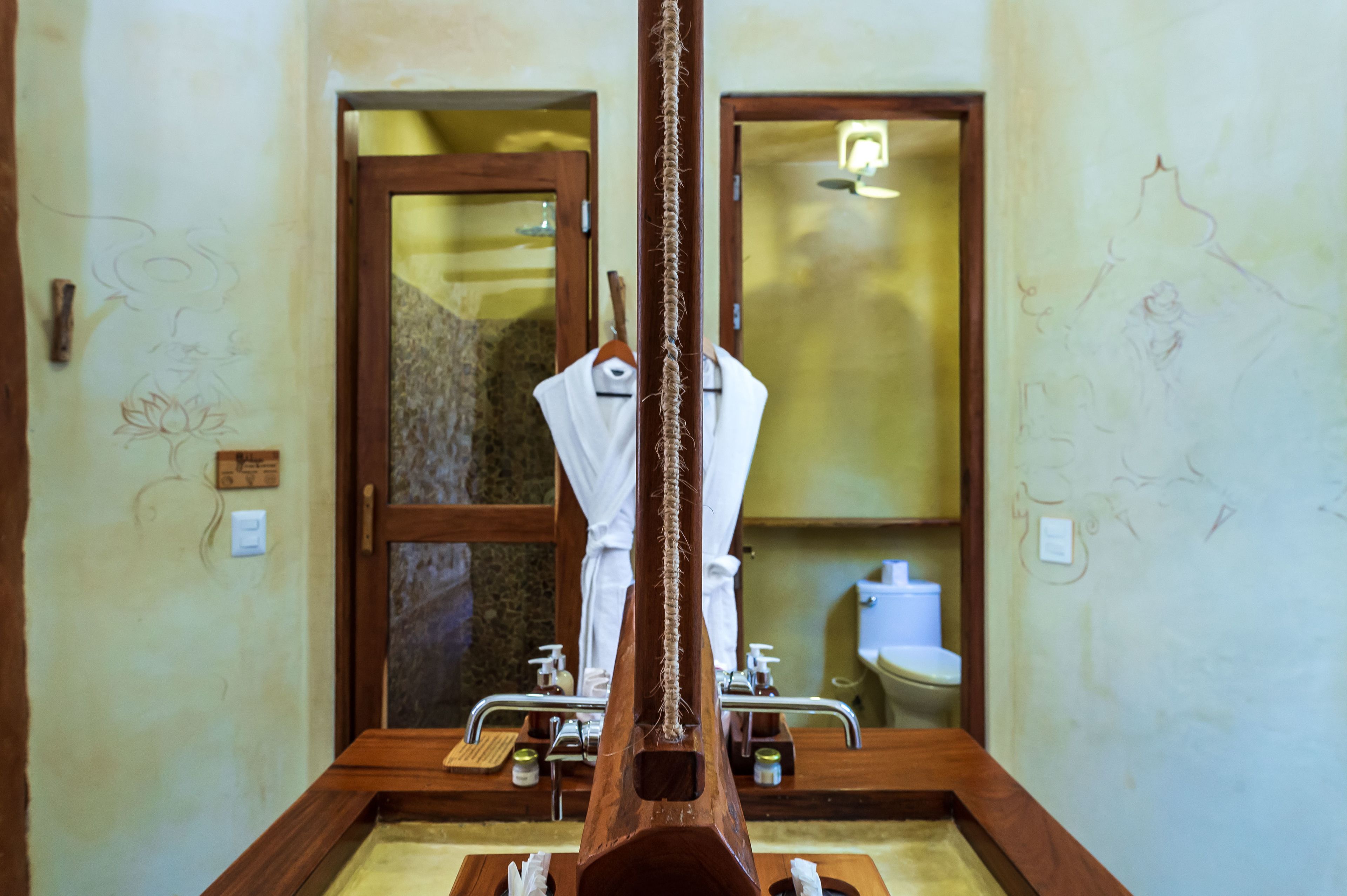 A bathroom with a wooden bathtub, a white towel, and a mirror reflecting a toilet and sink.