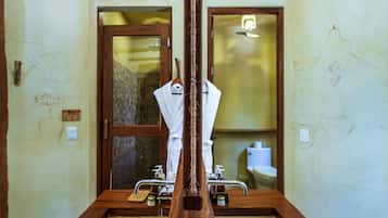 A bathroom with a wooden bathtub, a white towel, and a mirror reflecting a toilet and sink.