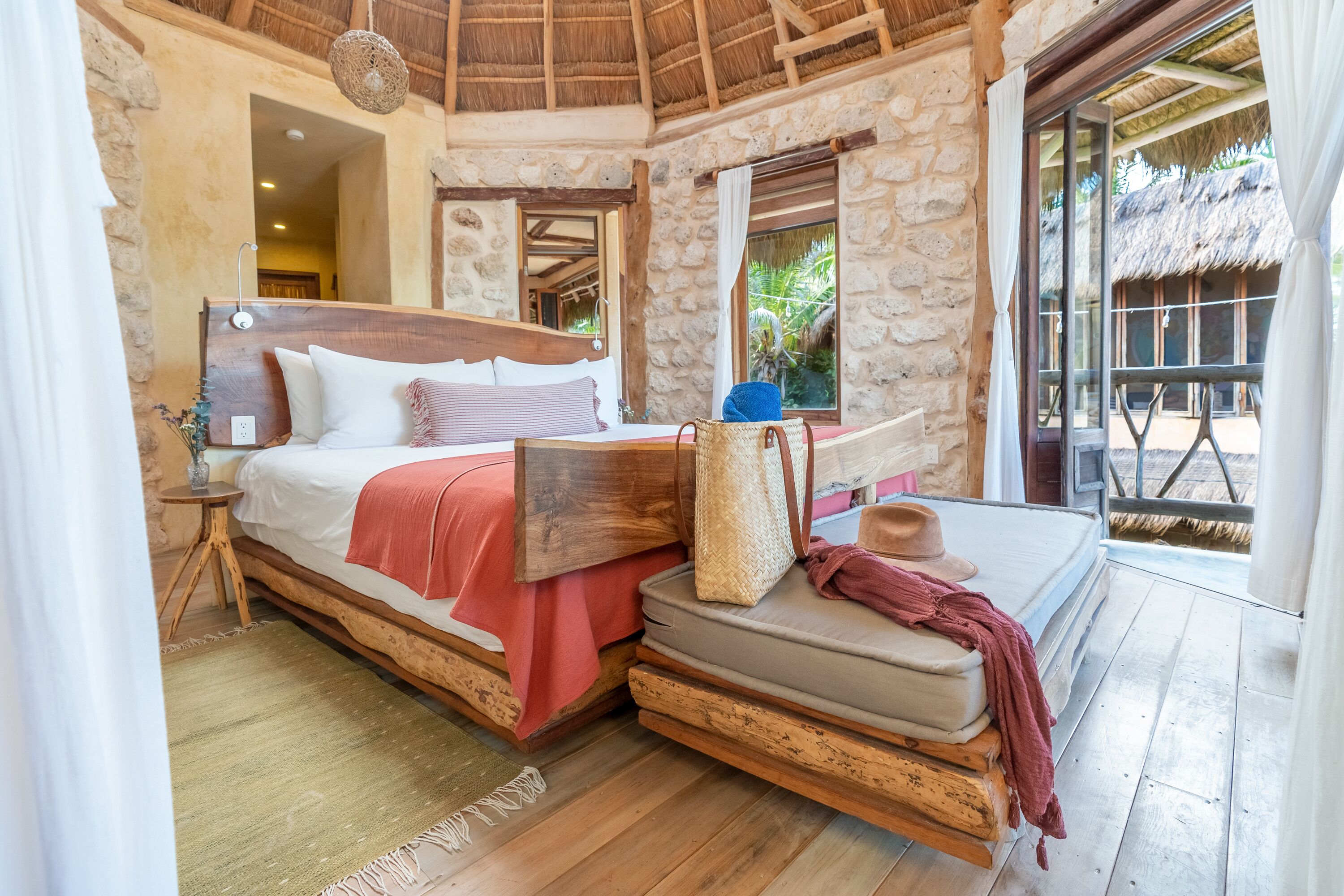 A rustic bedroom with a wooden bed, stone walls, and a thatched roof.