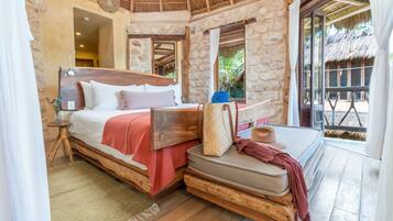 A rustic bedroom with a wooden bed, stone walls, and a thatched roof.