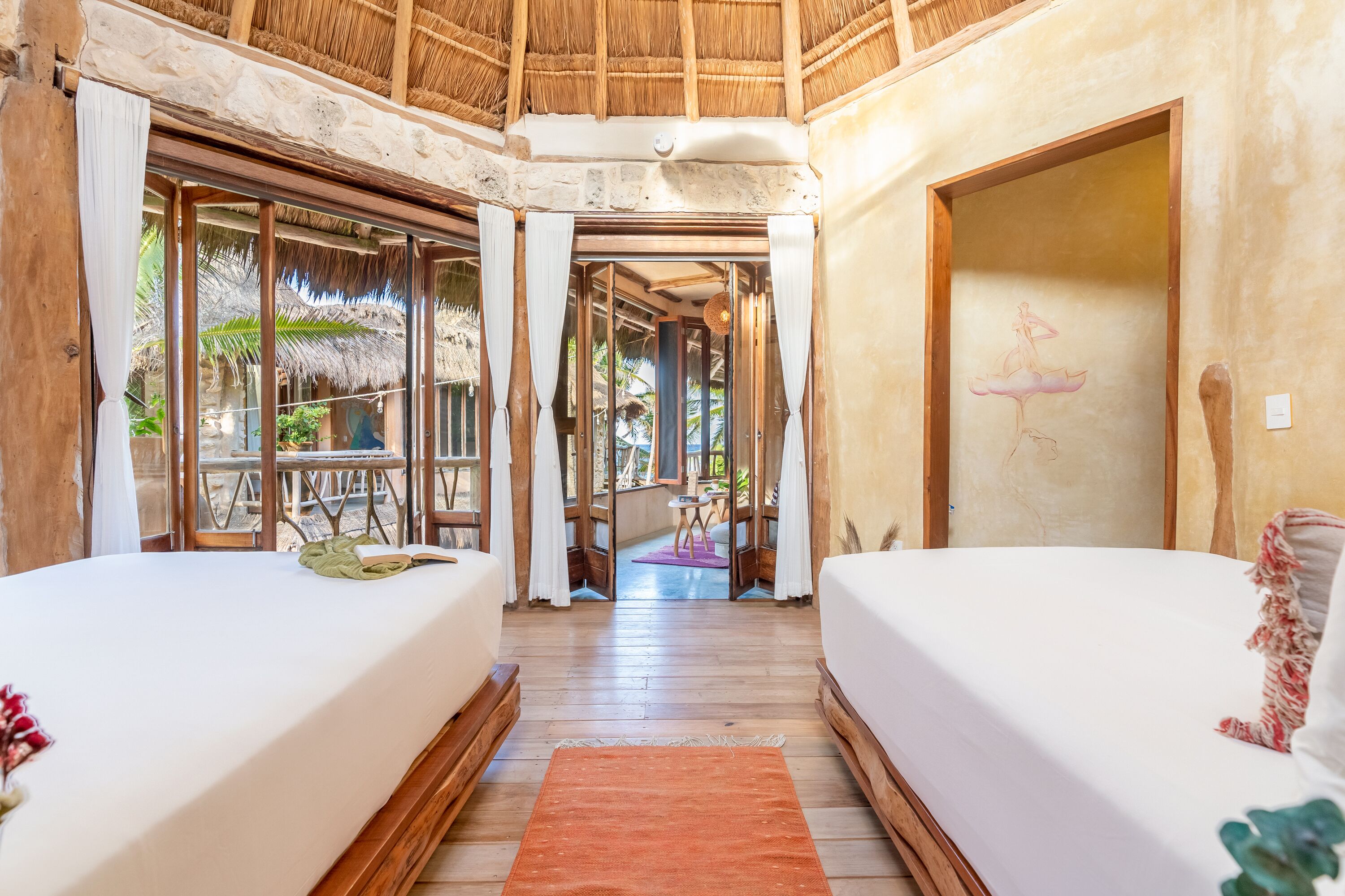 A room with two beds, a wooden floor, and a thatched ceiling.