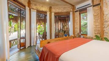 A room with a bed, wooden beams, stone walls, and a view of the outdoors.