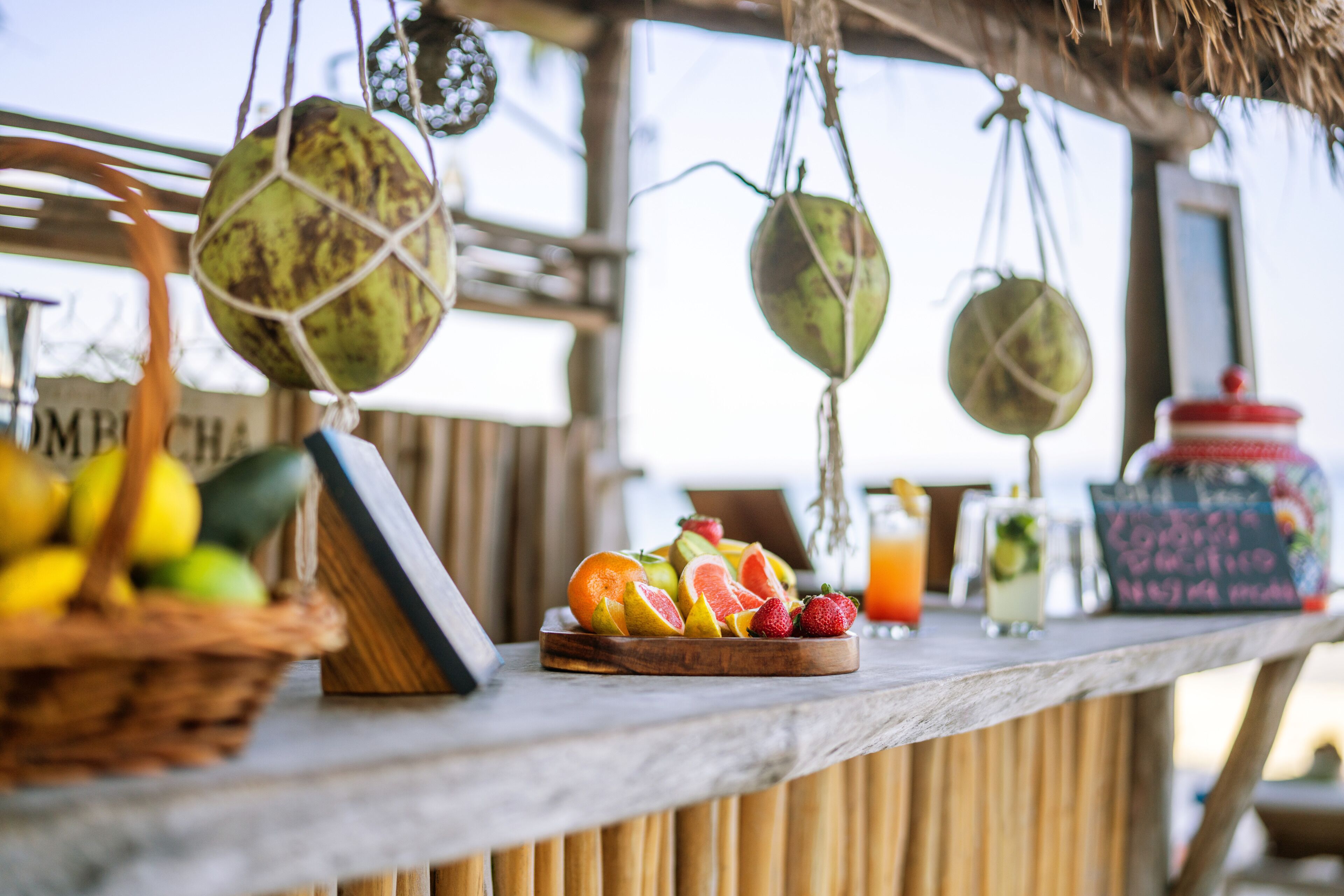 A wooden bar with a fruit display, hanging decorations, and a chalkboard menu.