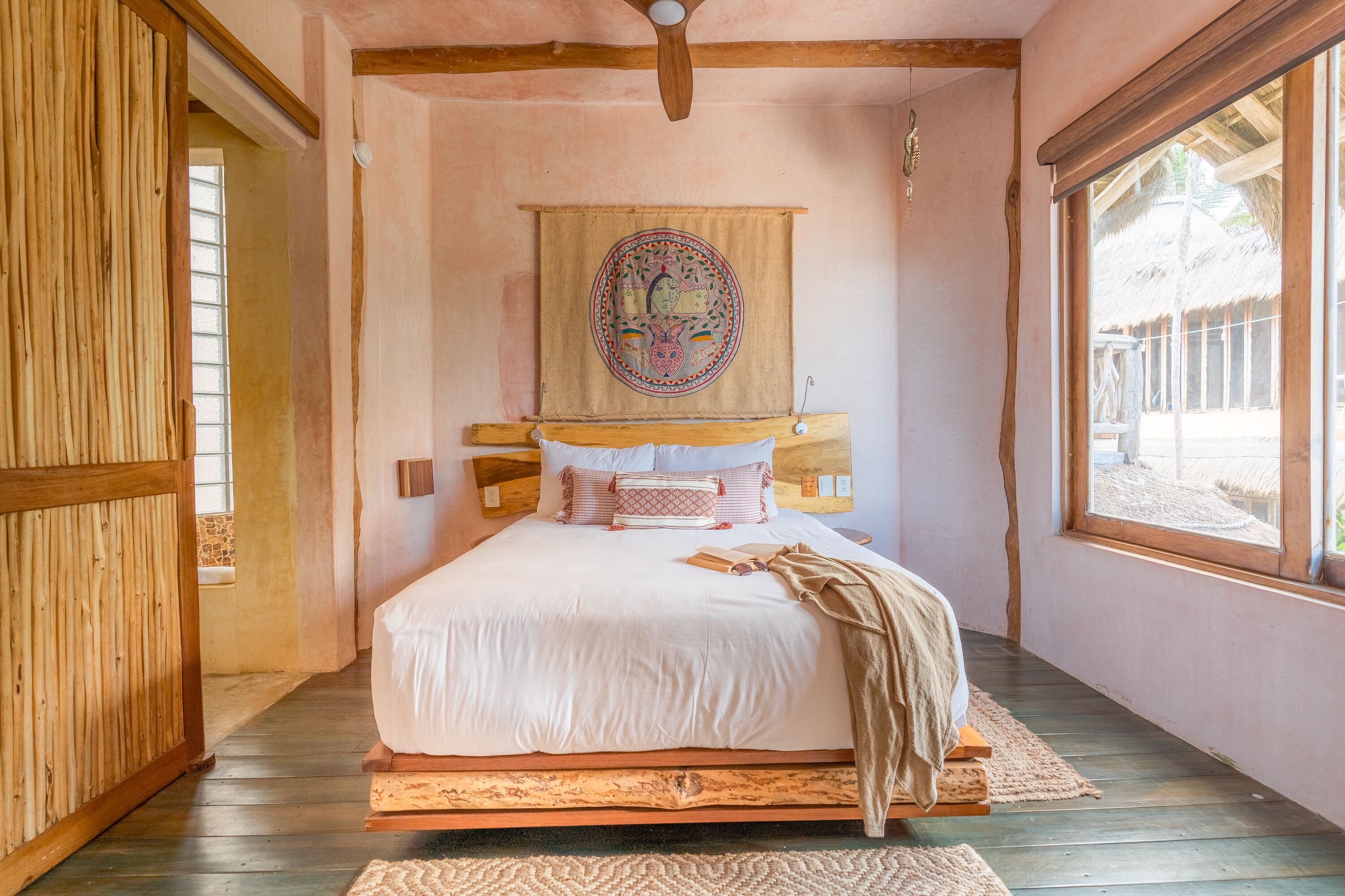 A bedroom with a wooden bed, a large window, and a hanging tapestry.