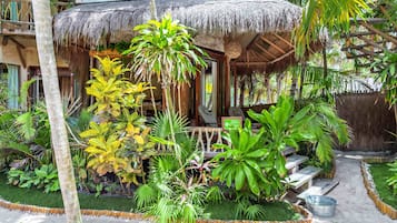 A tropical resort with a thatched-roof structure, lush greenery, and a small outdoor seating area.