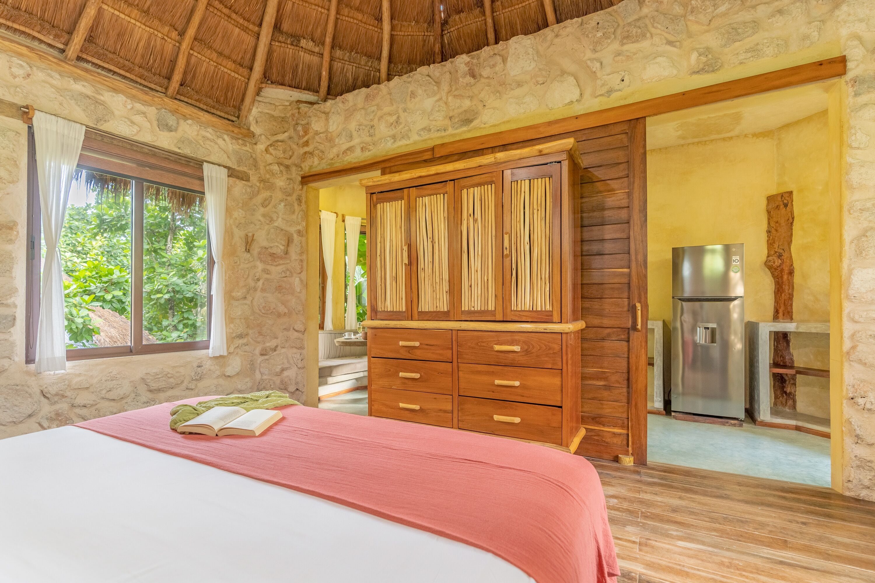 A bedroom with a bed, wooden wardrobe, and a view of a kitchen.