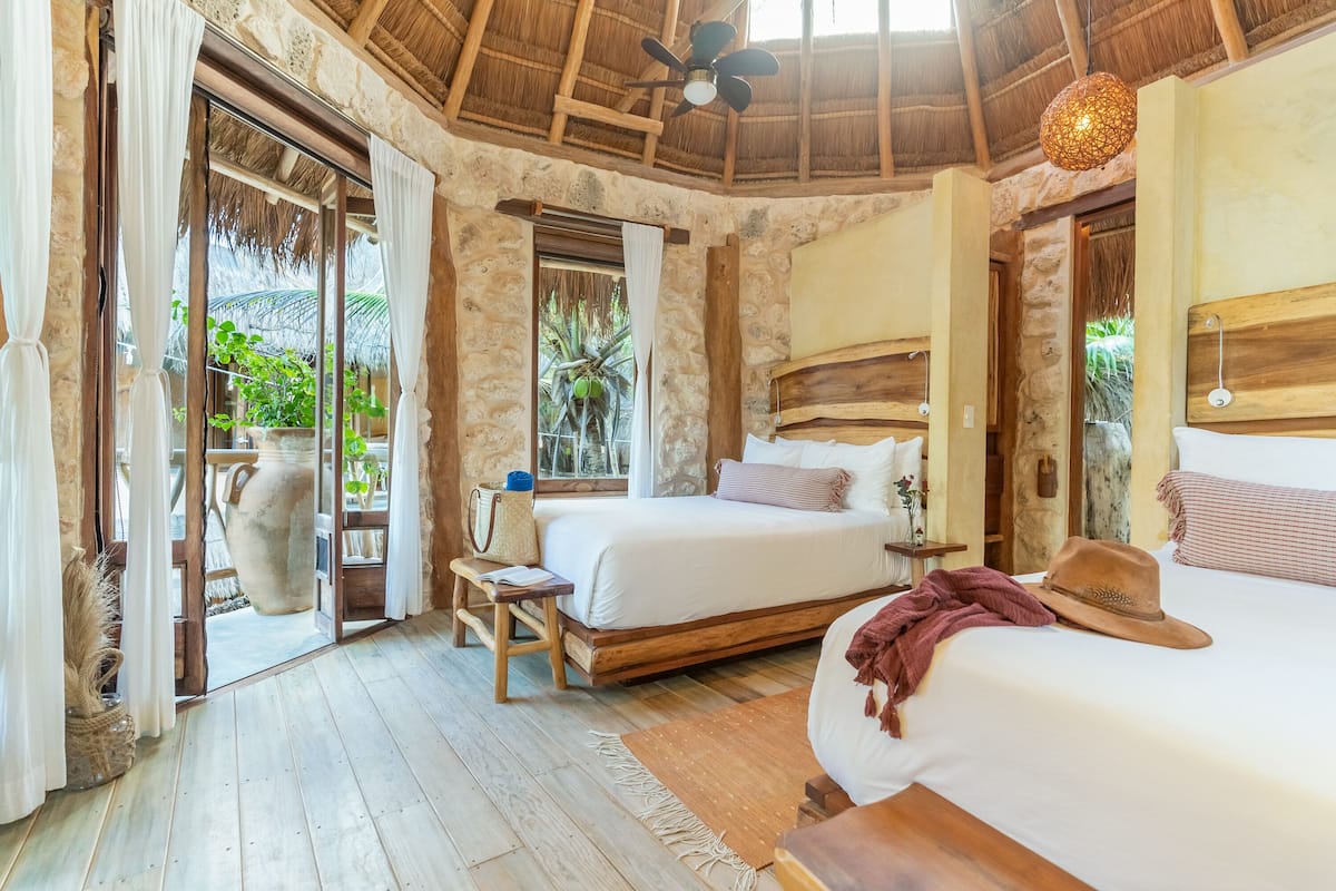 Una habitación con cama, mesitas de noche, ventilador de techo y vistas al exterior.