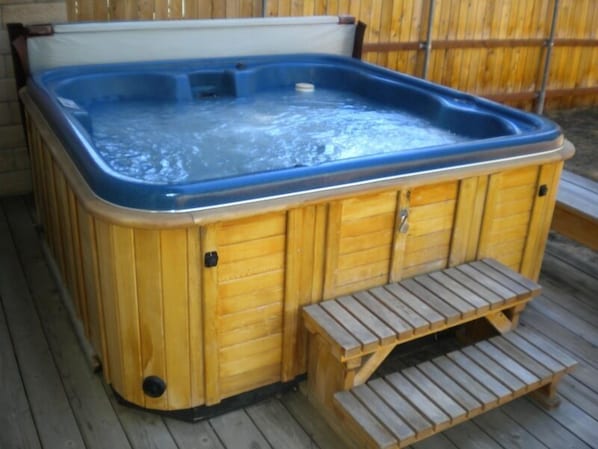 Un bain à remous en bois, doté d’un banc intégré et d’une marche facilitant l’accès.