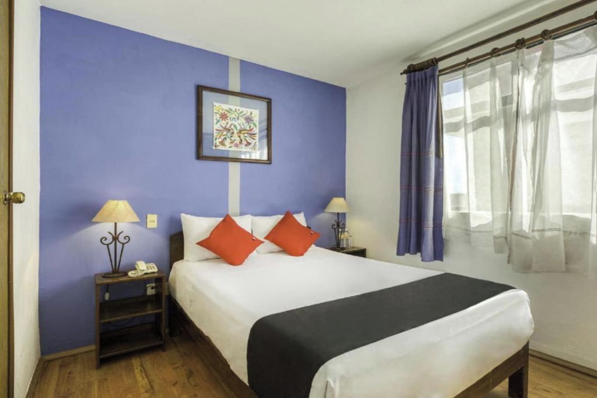 A hotel room with a large bed, two bedside tables with lamps, a framed artwork on the wall, and a window with curtains.