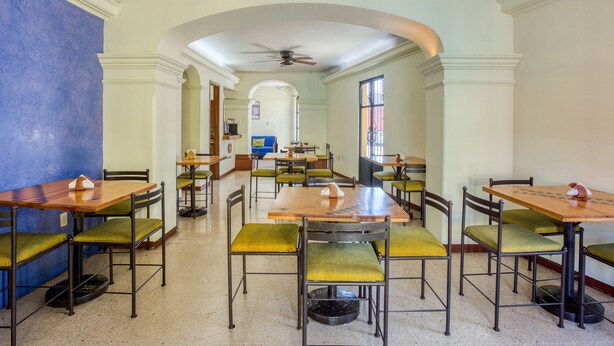 Comedor con varias mesas y sillas, un ventilador de techo y vista a través de un arco.