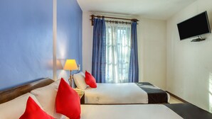 Una habitación de hotel con dos camas, televisión, lámpara y ventana con cortinas.