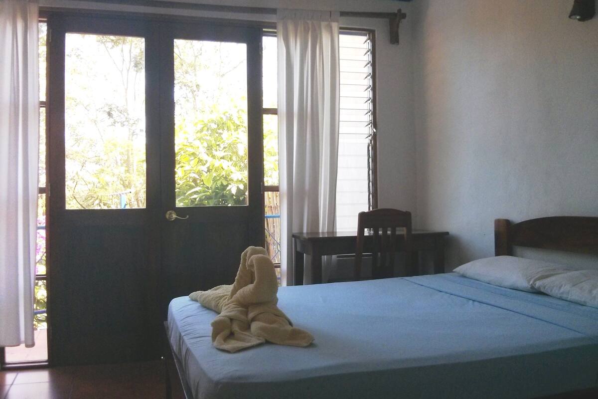 A bedroom with a bed, a chair, and a window with curtains.