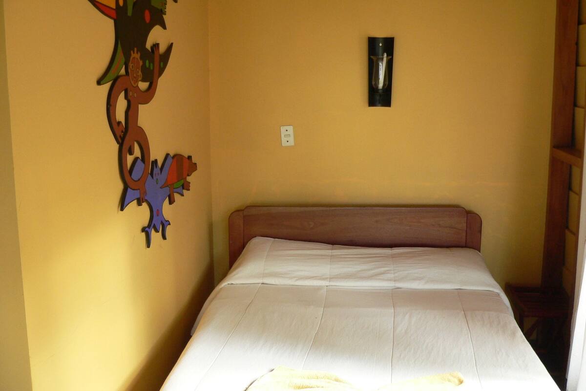 A bedroom with a bed, a wall-mounted light fixture, and a decorative wall piece.