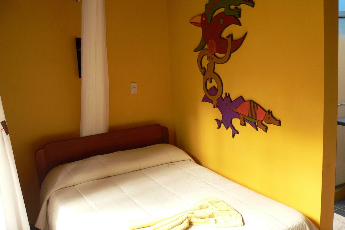 A single bed with a white mattress and a red headboard in a room with yellow walls.