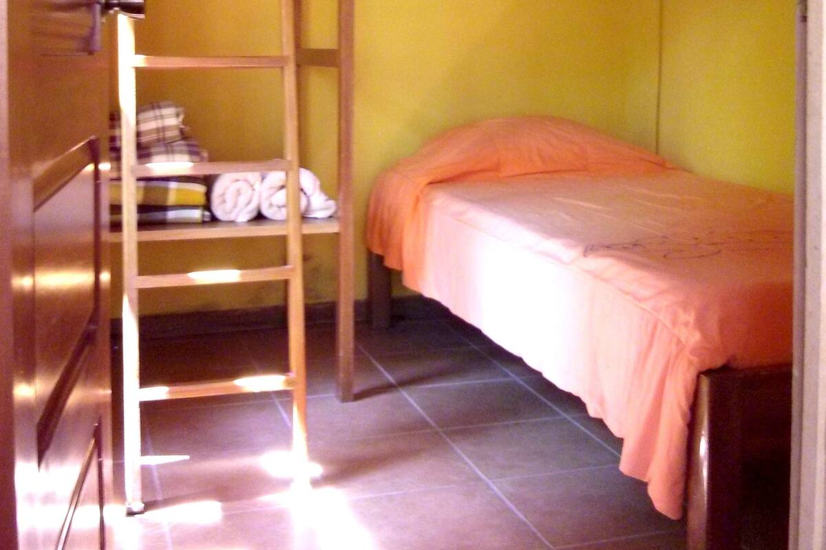 A bunk bed room with a ladder, a mosquito net, and a shelf with folded towels.