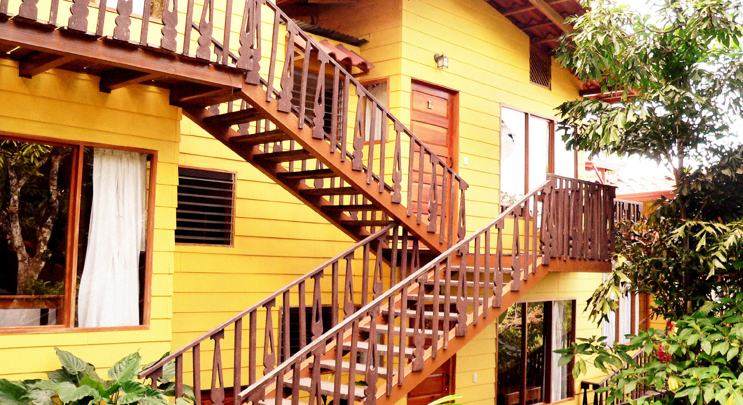 A yellow building with a wooden staircase leading to a balcony.