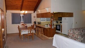 A compact kitchen with a dining area, a small bar, and a bed with floral bedding. - 835 Paloma Ave. (South Lake Tahoe)
