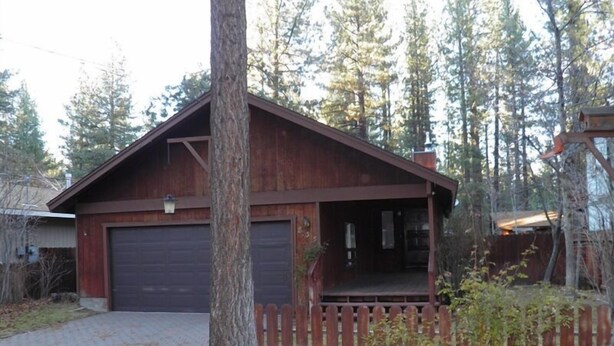 A rustic cabin with a garage, a porch, and a wooden fence. - 835 Paloma Ave. (South Lake Tahoe)
