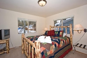 A bedroom with a wooden bed frame, a quilted bedspread, a television on a small table, and a window with a view of a snowy landscape. - 2853 Springwood Dr. (South Lake Tahoe)