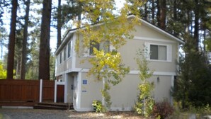 A two-story house with a front porch, surrounded by trees and a wooden fence. - 2853 Springwood Dr. (South Lake Tahoe)