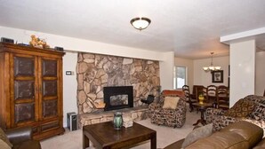 A living room with a stone fireplace, leather sofas, a wooden cabinet, and a dining area with chairs and a table. - 2853 Springwood Dr. (South Lake Tahoe)