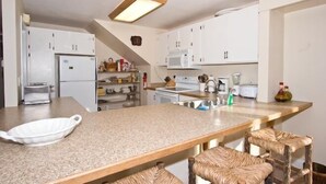 A kitchen with white cabinets, a granite countertop, a microwave, a stove, and wicker bar stools. - 2853 Springwood Dr. (South Lake Tahoe)