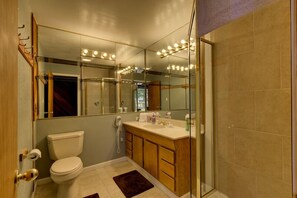 Et moderne badeværelse med glasvæg omkring bruseren, et vaskebord med spejl og et toilet.