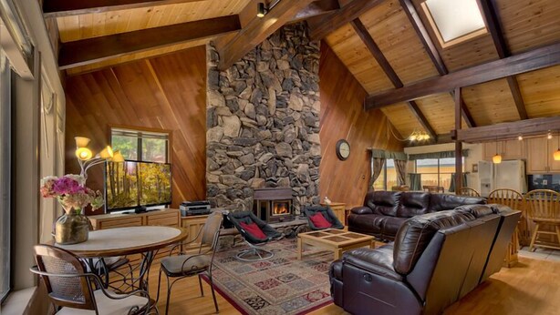 A cozy living room with a stone fireplace, leather sofas, and a dining area with a table and chairs. - 3042 Sierra Blvd. (South Lake Tahoe)