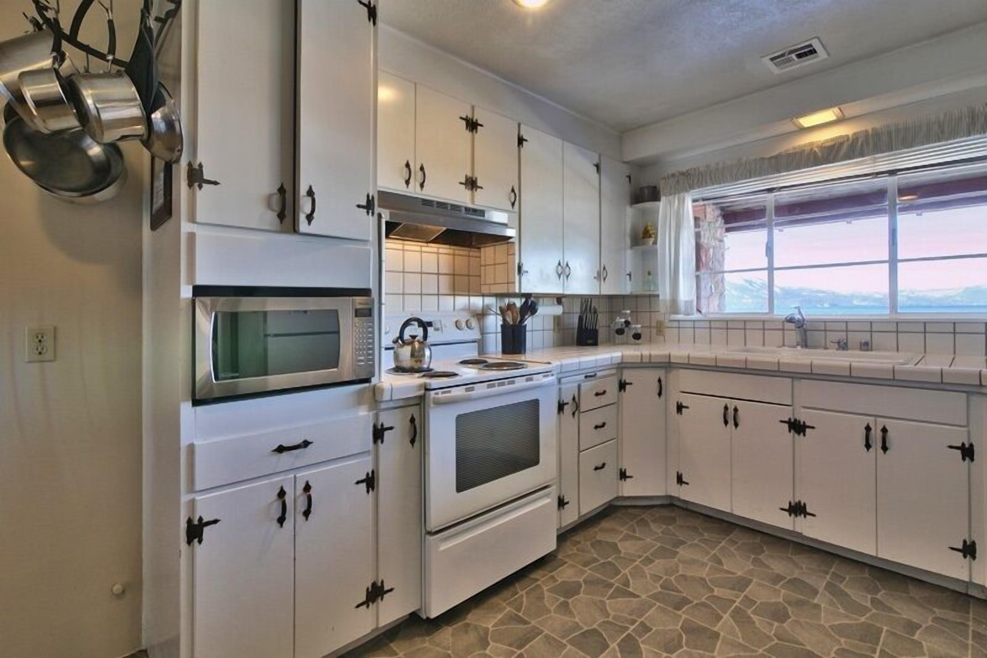A kitchen with white cabinets, a microwave, stove, and a window with a view.