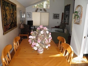 Uma sala de jantar com uma mesa e cadeiras de madeira, um vaso com flores e um quadro na parede.