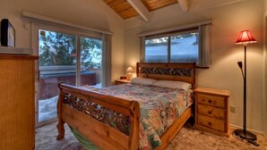 A bedroom with a wooden bed, a nightstand, a lamp, and a sliding glass door leading to a balcony. - 3851 Saddle Road (South Lake Tahoe)