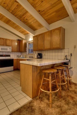 A kitchen with wooden cabinets, a white countertop, and a central island with stools. - 3851 Saddle Road (South Lake Tahoe)