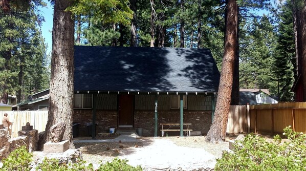 A small, rustic cabin with a dark roof, surrounded by tall trees.