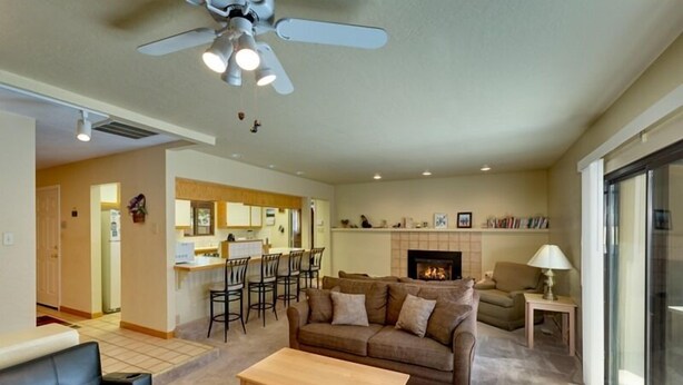 A living room with a sofa, a coffee table, and a fireplace. There is a kitchen area in the background with a dining table and chairs. - 3221 Marlette Circle (South Lake Tahoe)