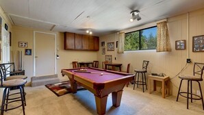 A pool table in a room with a ceiling fan, wooden cabinets, and a window with curtains. - 3221 Marlette Circle (South Lake Tahoe)