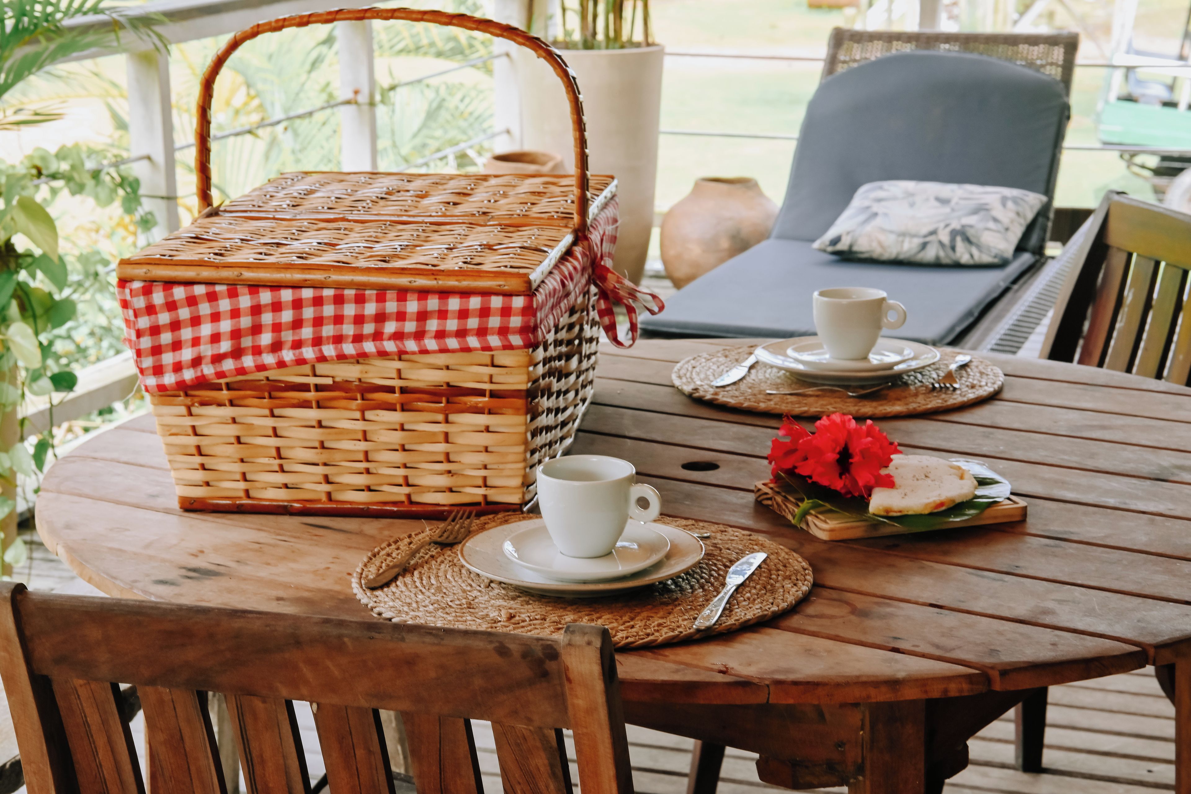 Un tavolo di legno con un'attrezzatura da picnic che include un cesto, tazze, piatti e un fiore.