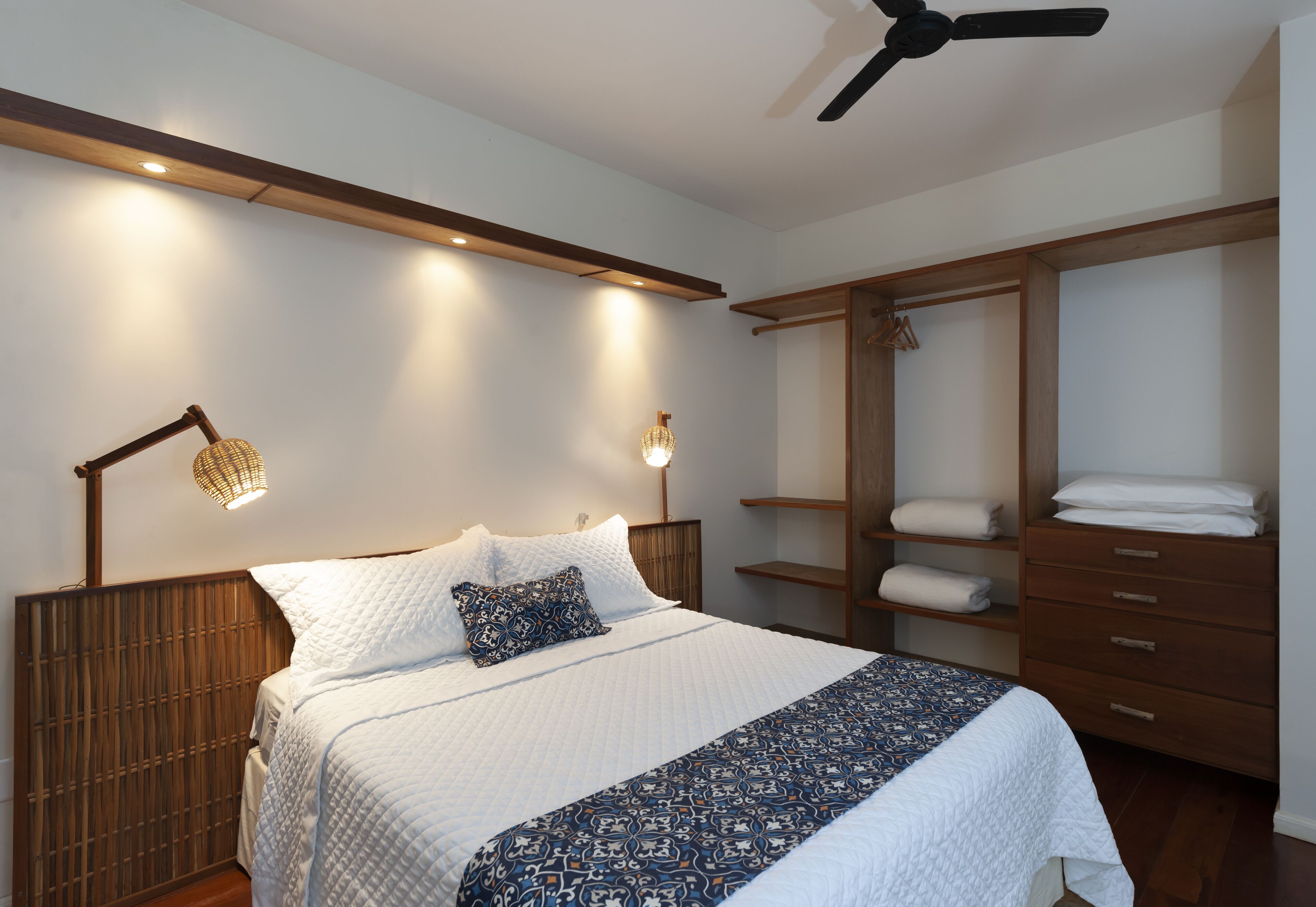 A bedroom with a bed, bedside lamps, a wardrobe, and a ceiling fan.