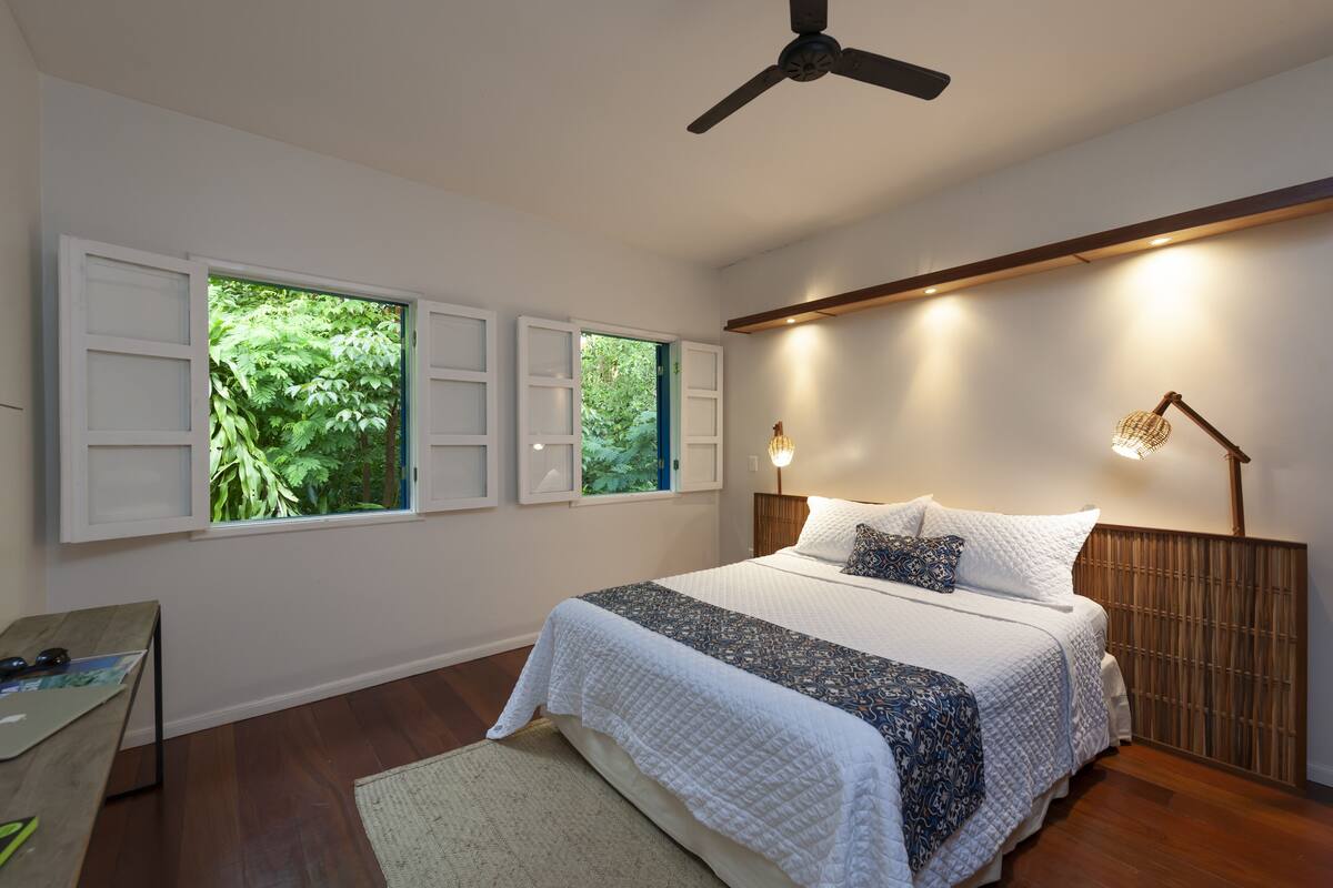 Un dormitorio con cama, escritorio y dos ventanas con contraventanas.
