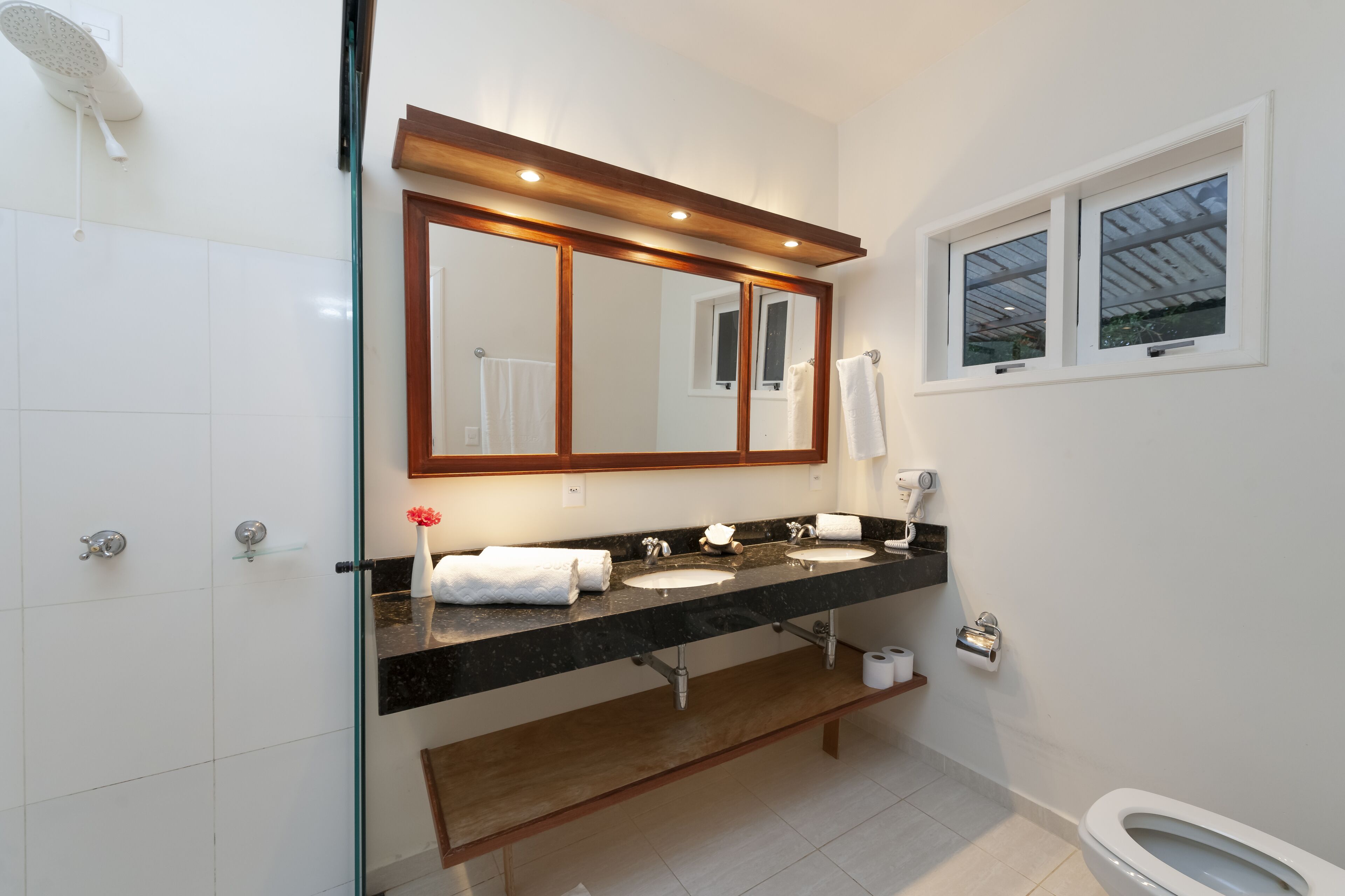 A bathroom with a glass shower enclosure, a double sink vanity, a large mirror, and a toilet.