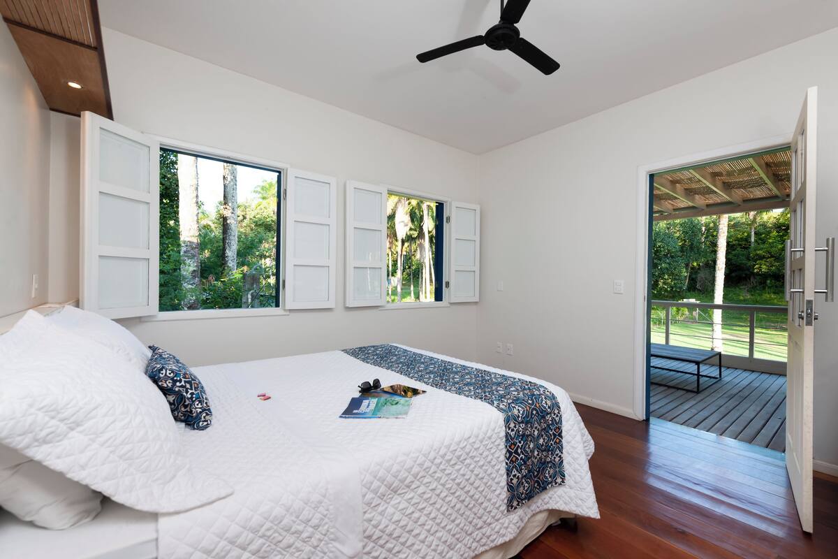 Un dormitorio con cama, ventilador de techo y vistas a una terraza y follaje exterior.