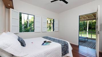 Ein Schlafzimmer mit Bett, Deckenventilator und Blick auf eine Terrasse und Grünfläche.